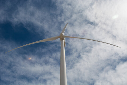 Low angle shot of a clean modern white wind turbine propeller rising into a deep blue clear sky.