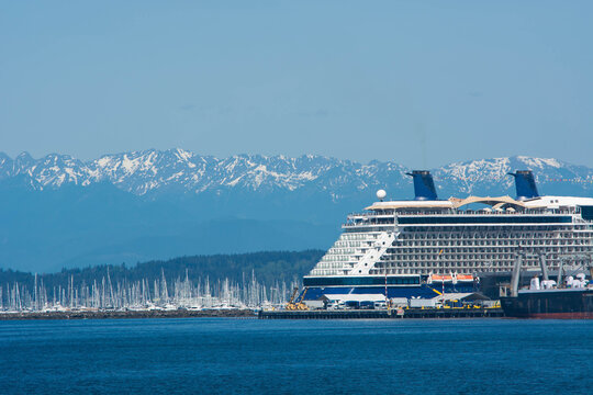Large cruise ship docked at a port terminal with the snow-covered Olympic Mountain range rising majestically in the background.