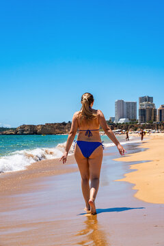 Beach vacations in Portimao, Portugal. Beautiful middle-aged woman walking on sandy beach Praia da Rocha in summer. Back view