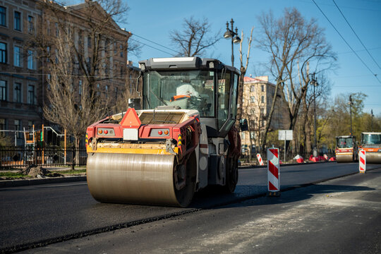 Orange road roller on street compacts freshly laid asphalt on traffic road, construction works in modern city, heavy machinery in action to pave driveway, roller smoothing surface to prevent damage.