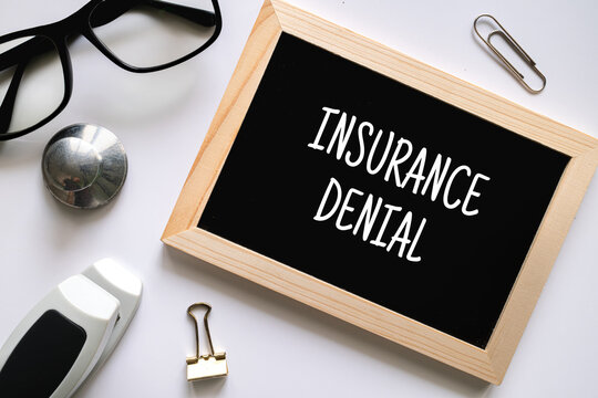Insurance Denial text on black chalkboard with glasses and office supplies on white background, healthcare policy concept