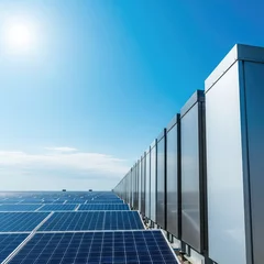 Large industrial battery storage units stand in a neat row under a bright sun, adjacent to a vast field of photovoltaic solar panels, charge, capacity, electrical © Chanchai