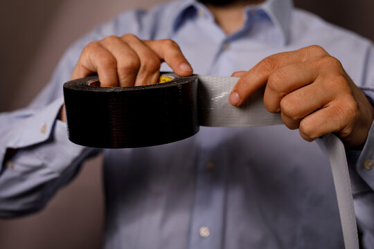 Close up of hands holding two rolls of duct tape, one black and one silver.