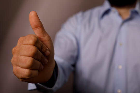 A man in a light blue shirt giving a positive thumbs up gesture for approval