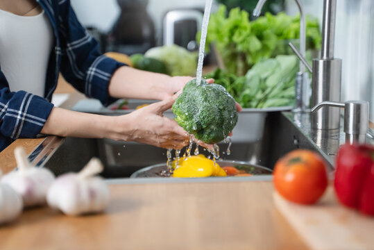 Close up of hands people washing vegetables by tap water at the sink in the kitchen to clean ingredient prepare a fresh salad.