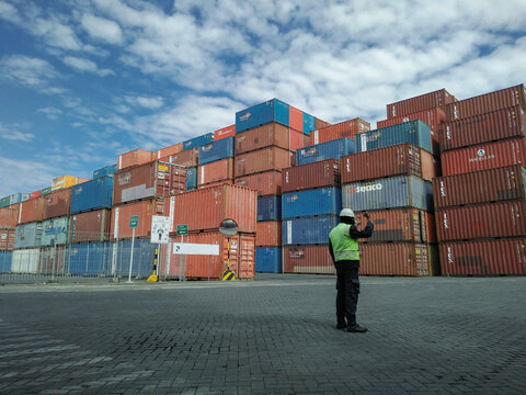 Stacked colorful metal shipping containers worker safety vest cloudy sky port terminal suitable for logistics, transportation, industrial, and portrelated concepts. Surabaya July 27th, 2020
