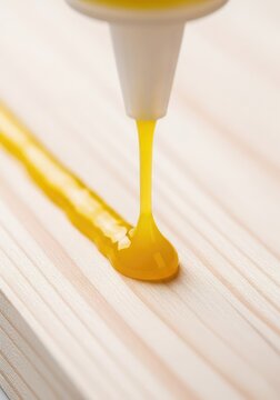 A stream of thick yellow adhesive is carefully applied from a plastic nozzle onto the surface of a light-colored natural timber board, glue, woodcraft, pva
