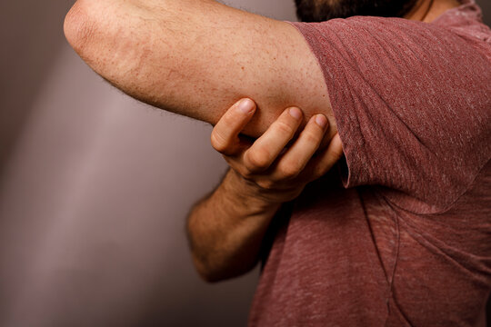 Close-up of a man holding his elbow due to sudden sharp pain and discomfort