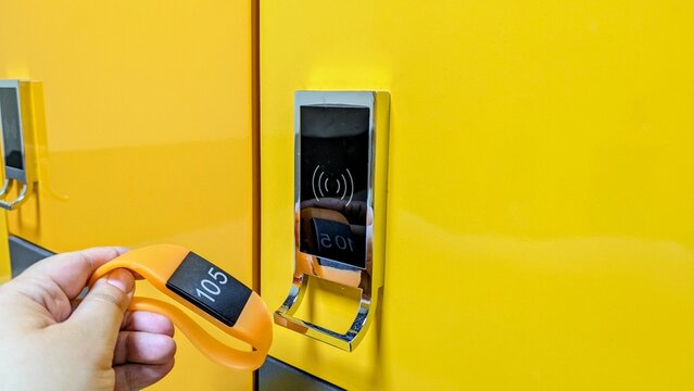 hand bringing an orange RFID wristband to a contactless electronic lock on a bright yellow locker in a changing room. Perfect for fitness, gym, spa, and security access concepts.