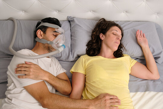 Man sleeping with CPAP machine while partner sleeps beside him in bed