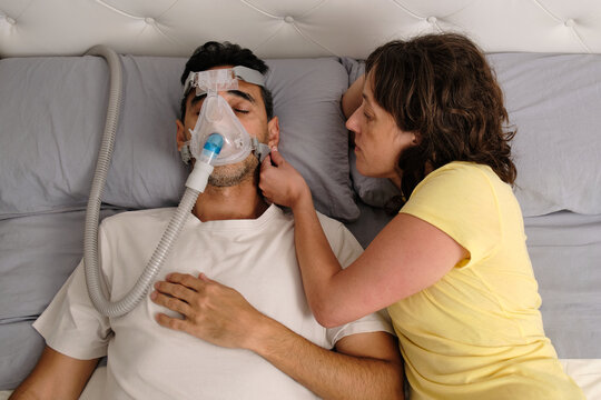 Woman adjusting CPAP mask on sleeping partner during sleep apnea therapy at home