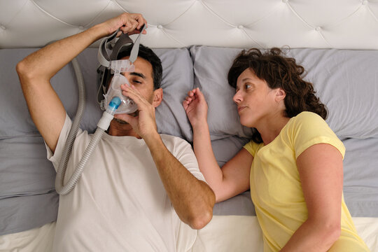 Man removing CPAP mask after waking up while partner watches in bed