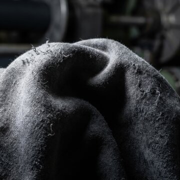 Close-up of Damaged Gray Knit Fabric with Pilling and Frayed Threads in Moody Industrial Setting for Textile Waste and Quality Control Messaging
