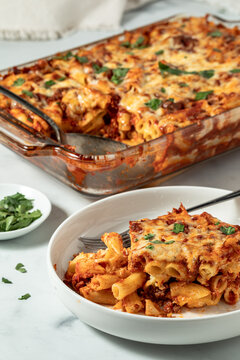 A serving of baked ziti with the full dish in behind, garnished with parsley.