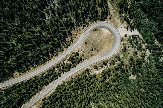 Aerial top down view of cars on curve high mountain asphalt road among green trees, sunny day