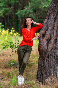 Woman in Red Blouse Leaning on Tree in Forest