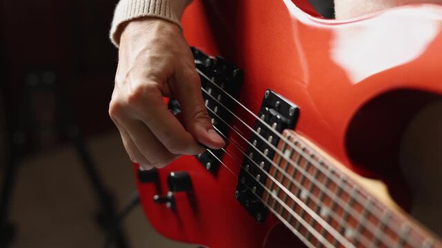 Close up view of woman playing orange electric guitar, practicing basic chords at home. Creative female musician holding plectrum and picking strings indoors. Music education and rehearsal concept.