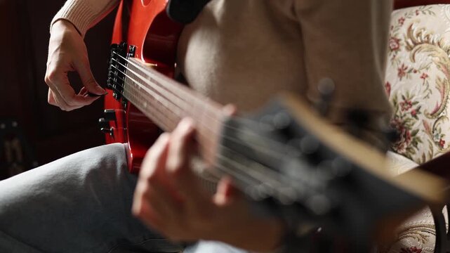 Close up view of woman playing orange electric guitar, practicing basic chords at home. Creative female musician holding plectrum and picking strings indoors. Music education and rehearsal concept.