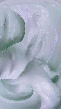 Top down view of cream being stirred slowly using a tool. Vertical video capture. Beauty product mixing process, smooth texture for skincare preparation.