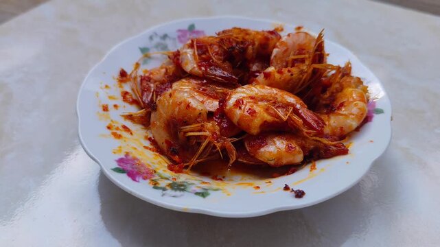 Close-up footage of spicy fried shrimp with red chili paste (udang balado) served on a floral plate, showcasing glossy texture and authentic Indonesian home cooking
