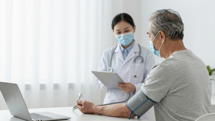 Fototapeta premium Nurse checking blood pressure of elderly patient