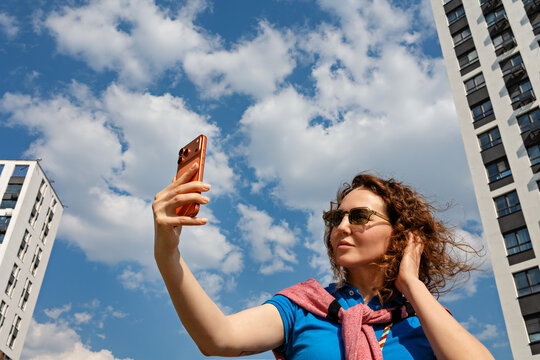 Woman takes selfie in city under blue sky