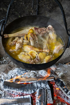 Outdoor cooking of poultry leg in a boiling cauldron over campfire
