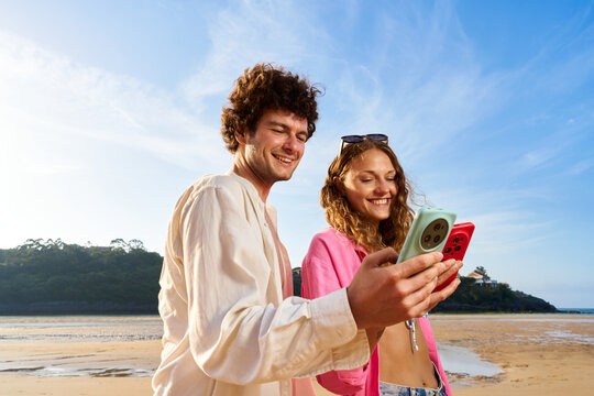 Happy couple using smartphone on beach browsing social media
