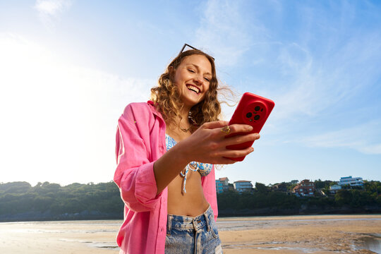 Young woman smiling while communicating with smartphone on beach