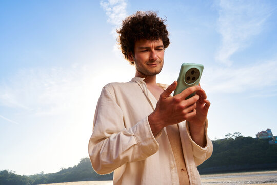 Man with curly hair using smartphone on beach