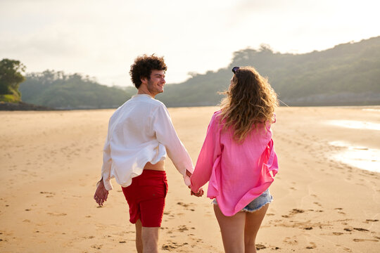 Couple holding hands walking on beach at sunset