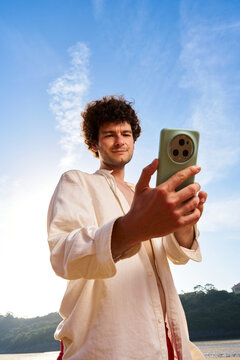 Curly man taking selfie with smartphone outdoors