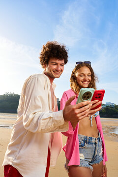 Smiling couple enjoying summer vacation sharing smartphones at beach