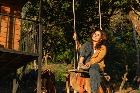 Young woman enjoying swinging near treehouse at sunset