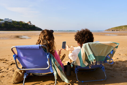 Couple relaxing on beach using smartphone during summer vacation