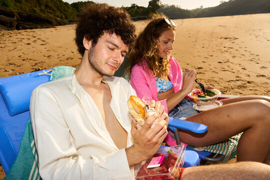 Young couple enjoying lunch eating sandwiches and salad on beach