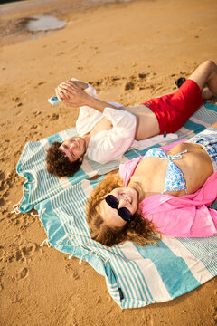 Young couple relaxing on beach towel using smartphone
