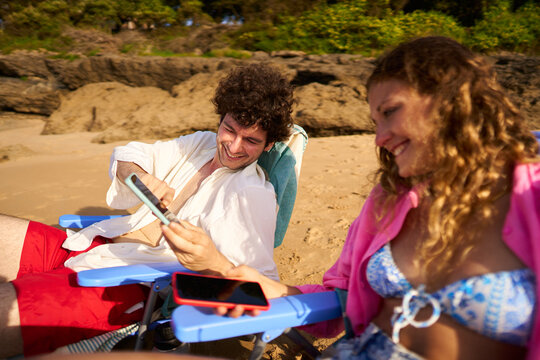 Couple laughing using smartphones relaxing on a beach vacation