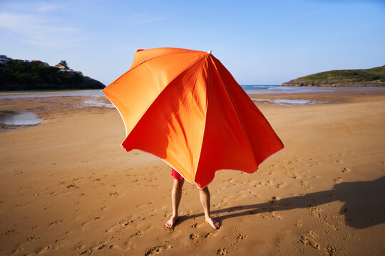 Person hiding under orange beach umbrella