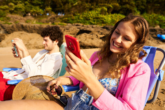 Couple relaxing on beach using smartphones and laughing