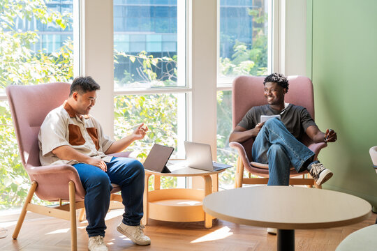 Two Men Talking in a Modern Lounge Area With Laptops and Natural Light