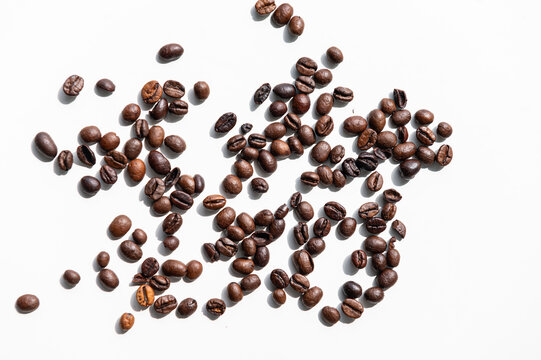 
Dark coffee beans scatter across bright white surface. Each bean shows natural curves and rich, glossy texture. Variations in color hint at different roast levels. 
