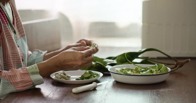 Close up. Asian Woman Hand Peeling Parkia Speciosa , Stink Bean, Bitter Bean, with Knife into White Plate on Table.