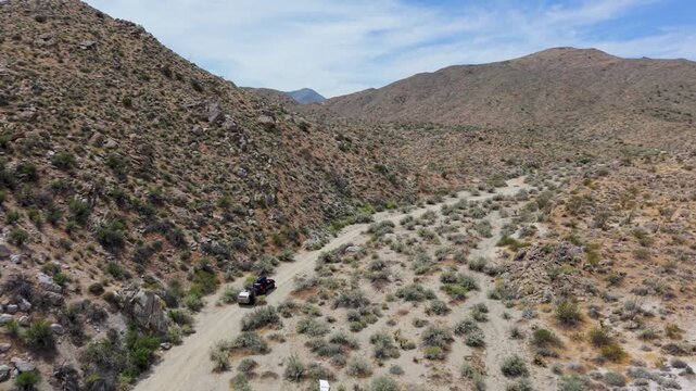A suv pulls a teardrop camper trailer through dirt trails in Anza Borego desert mountains during bright daylight hours.