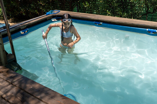 Girl With Goggles Cleaning A Backyard Pool With A Skimmer Pole