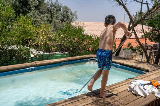 Kid Skimming A Backyard Pool With A Leaf Net On A Hot Summer Day