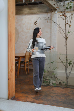 Woman walking in cafe holding coffee and laptop