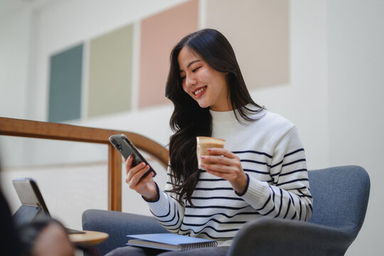 Young Asian woman smiling using smartphone drinking coffee