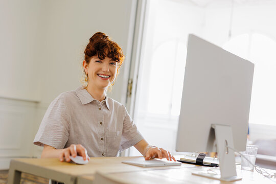 Professional woman smiling while working on computer at bright office