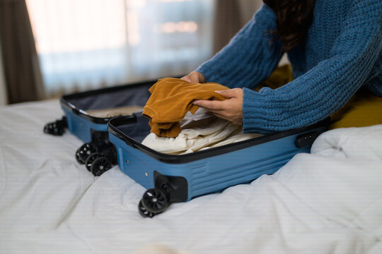 Person packing clothes into blue suitcase for travel